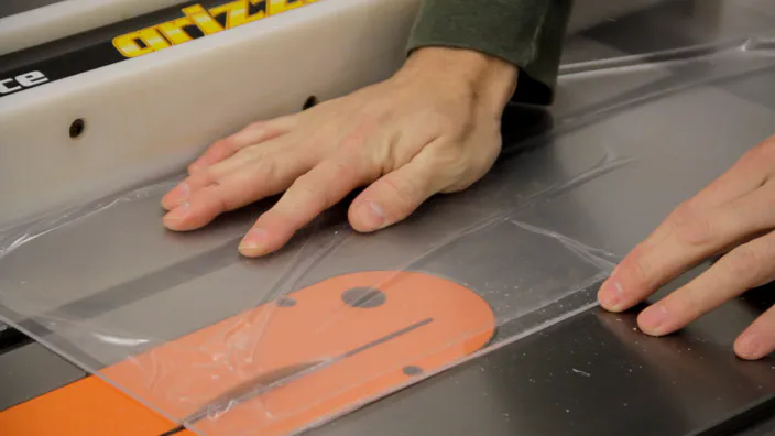 A sheet of clear acrylic is cut on a table saw.