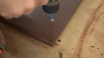 A drill is used to pre-drill holes in the underside of the top.