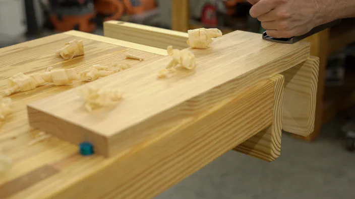 A plane is used on a board secured in between bench dogs.
